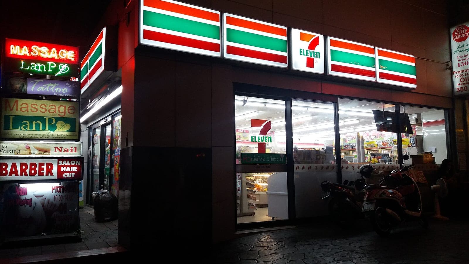 7-Eleven store in Bangkok at night next to massage and barber signs