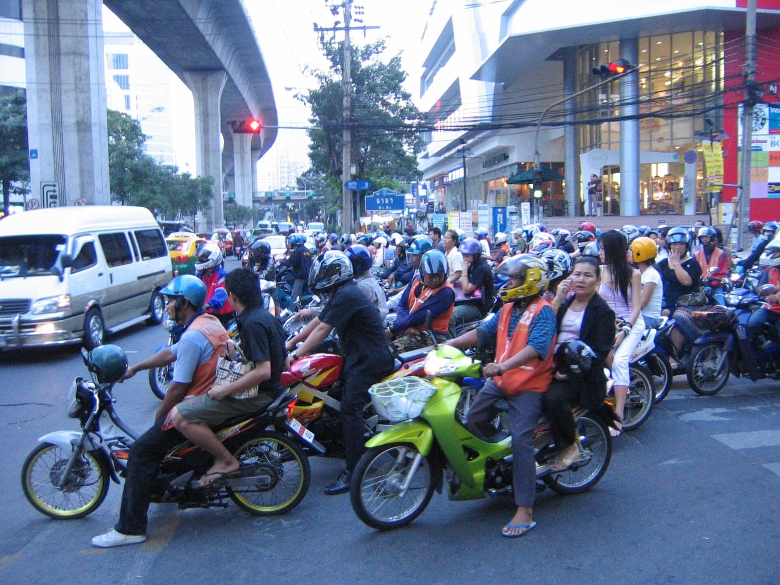 Motorbike taxi riders in orange vests waiting at a traffic light in Bangkok
