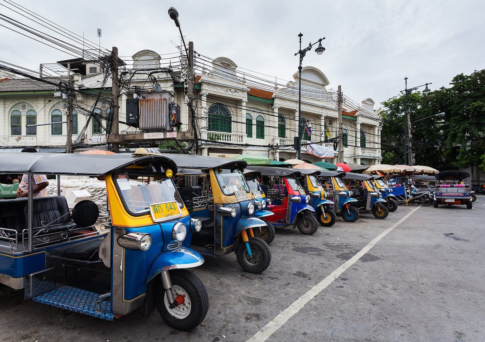 A row of blue and yellow tuk-tuks parked on a street in Bangkok