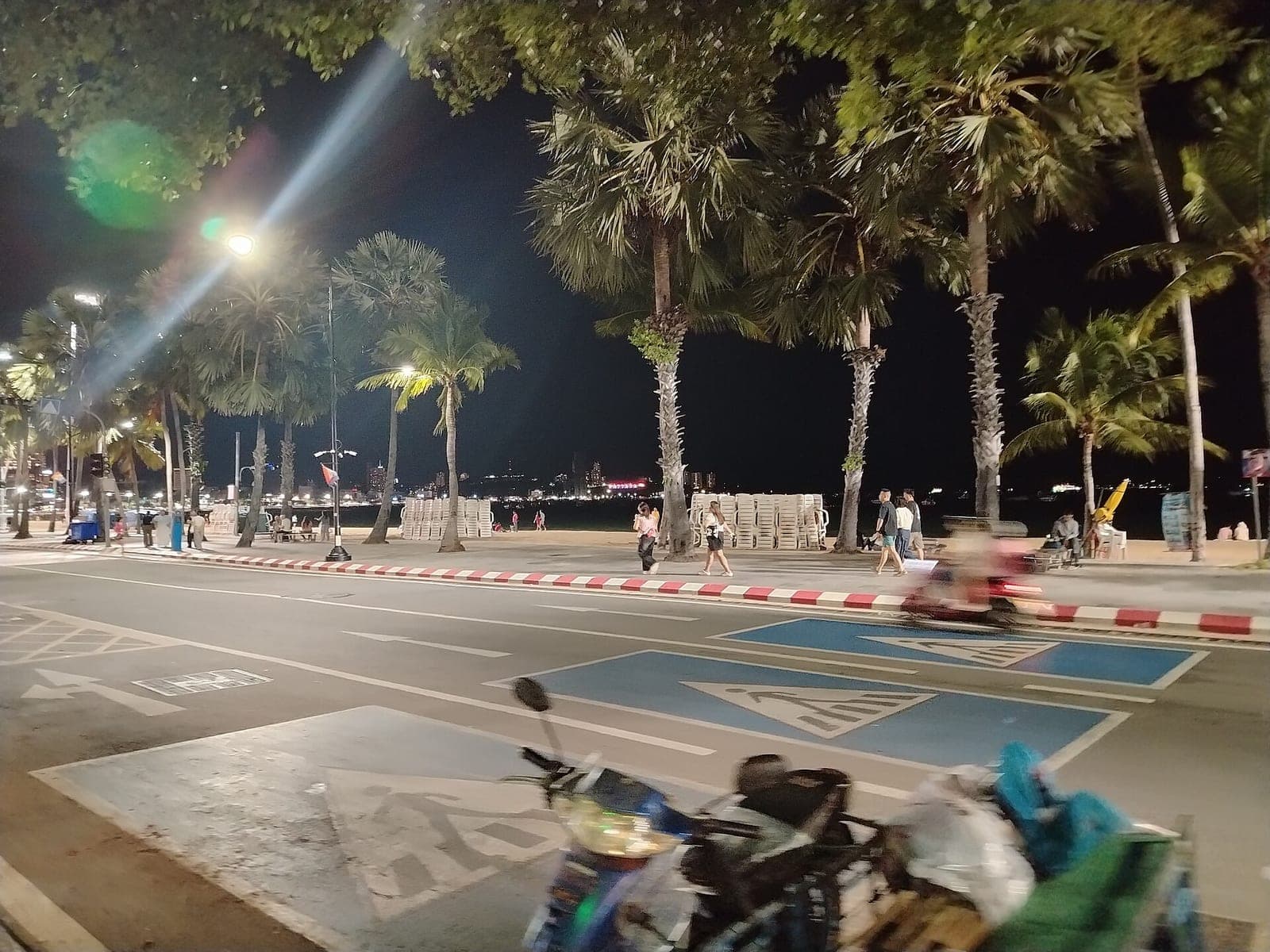 Beach Road, Pattaya, at night with palm trees, a passing motorbike and people on the promenade