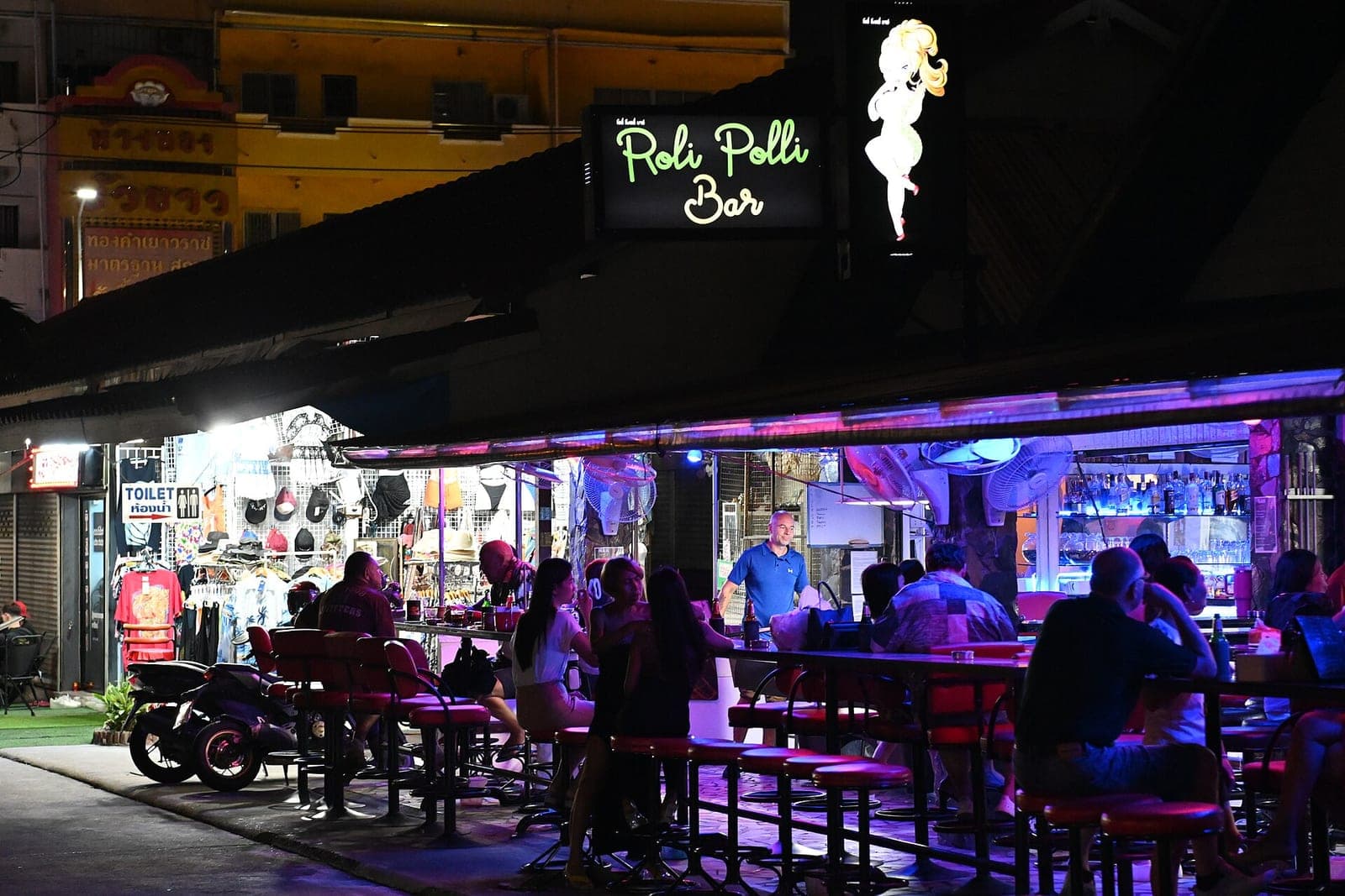Open-air bar in Pattaya at night with customers at tables under neon lights