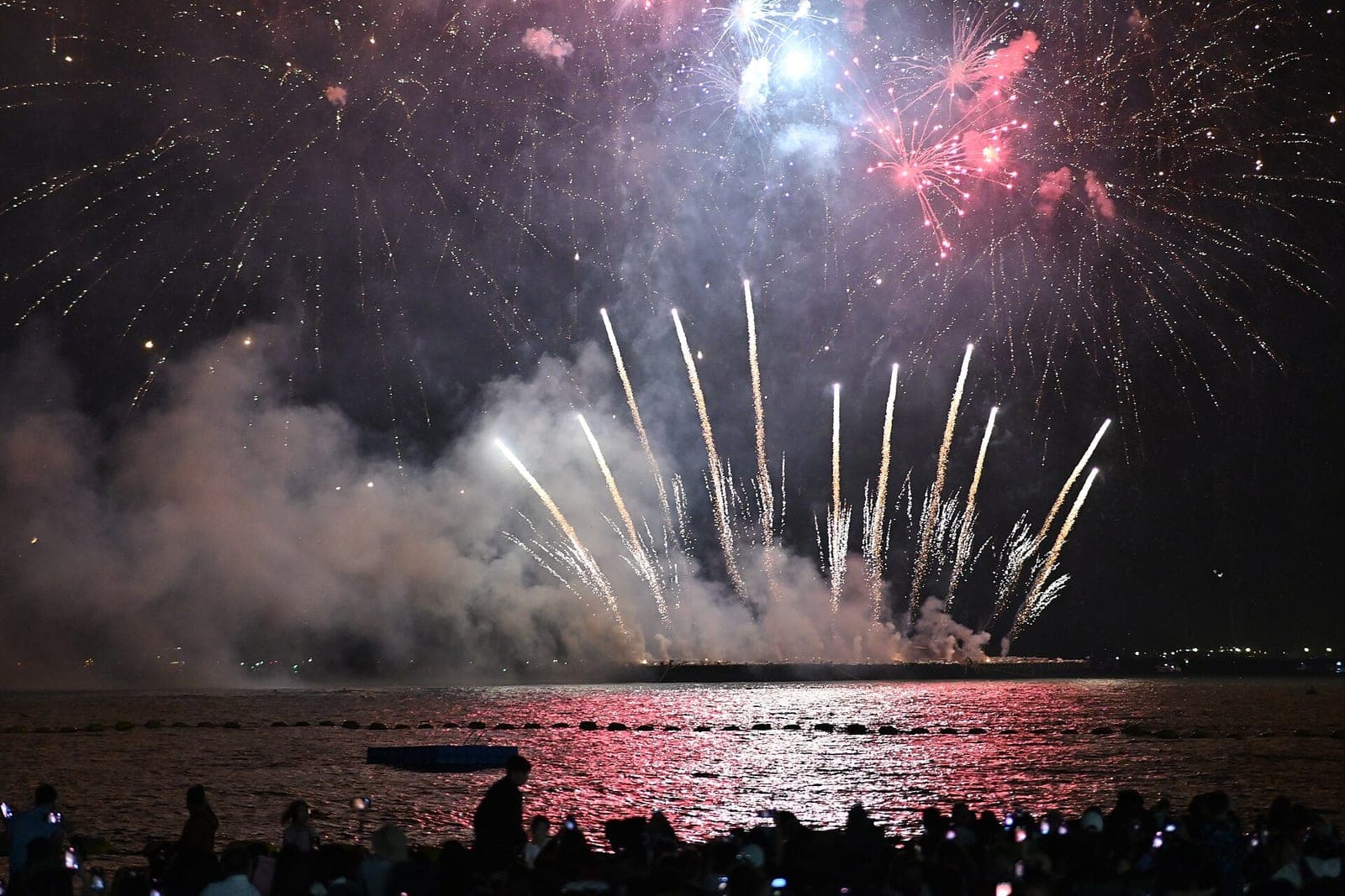 Fireworks over Pattaya Bay at night watched by a crowd on the beach