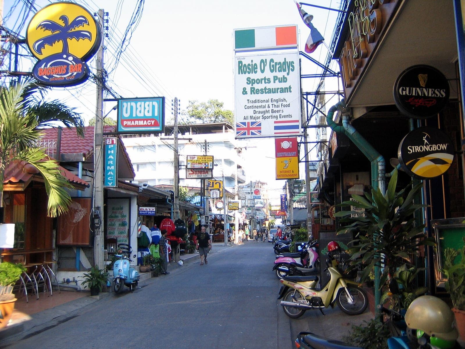 Soi 7, Pattaya, in daytime with bar and pub signs and parked scooters