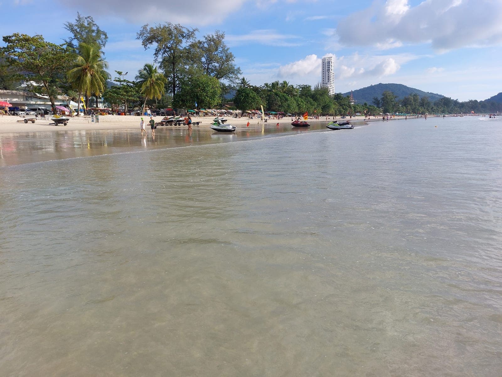 Patong Beach, Phuket, in daytime with jet skis, palms and the hills behind